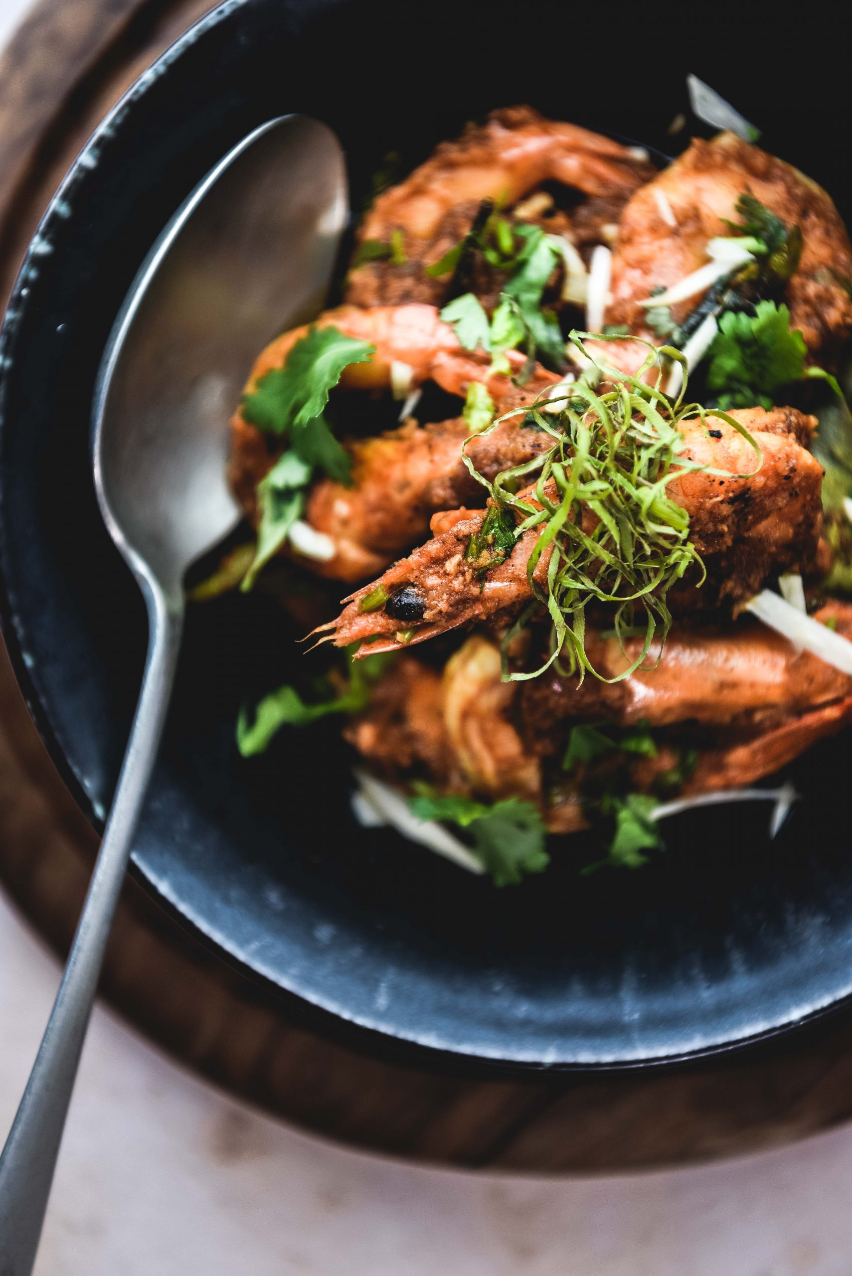 Prawns, silver spoon, black plate and wooden disk