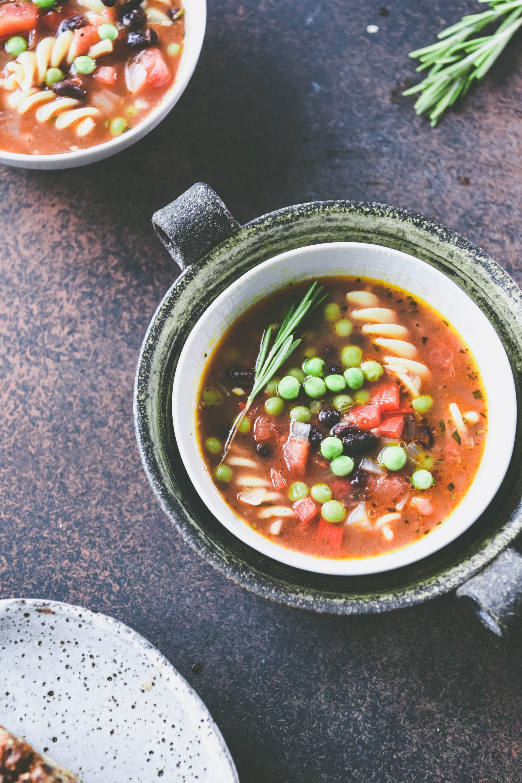 Two bowls of Black Bean and Pasta Soup, and a white plate. Itsa one-pot and easy meal.