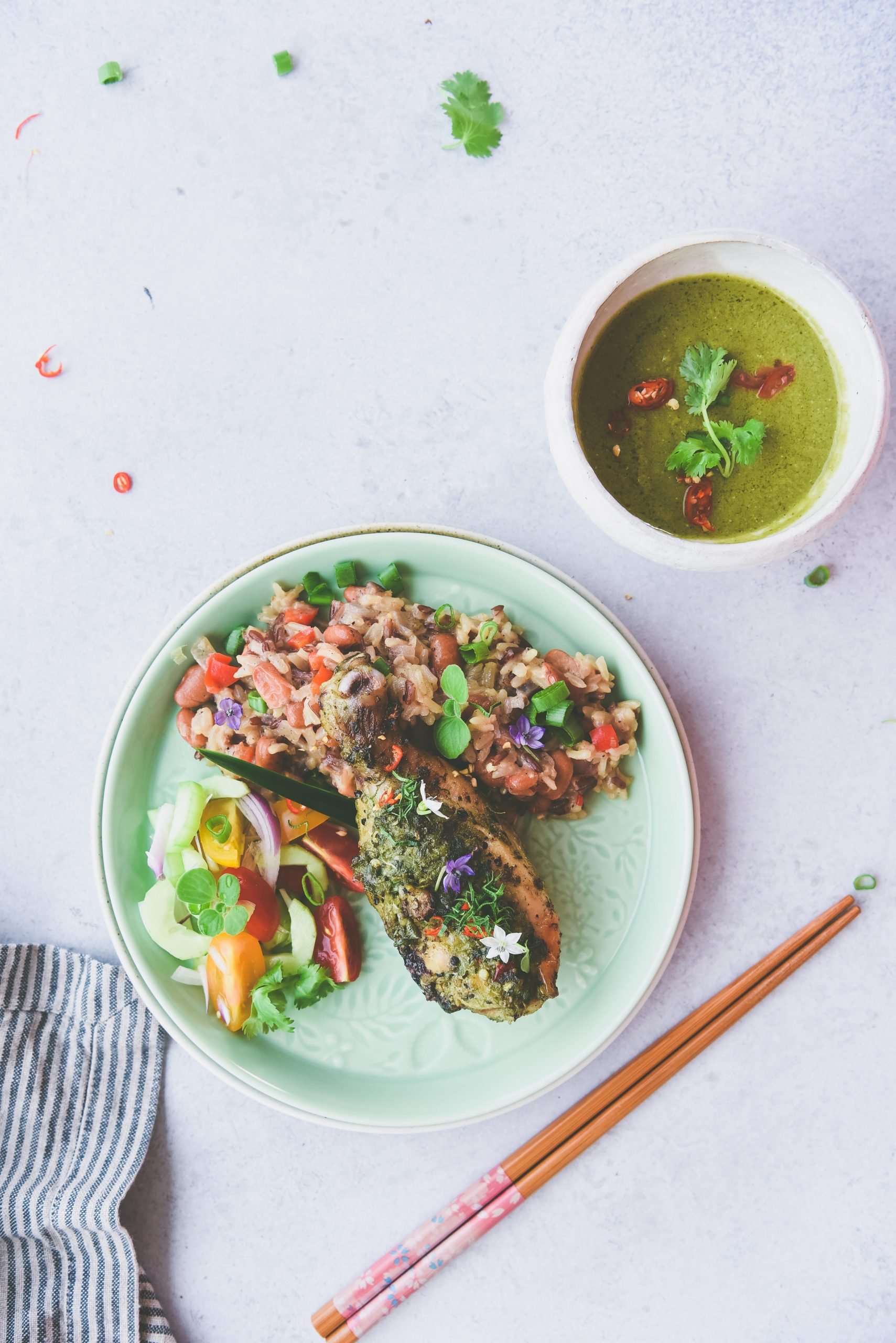 Strip grey napkin, chicken drumstick, chopstick, green plate and sauce